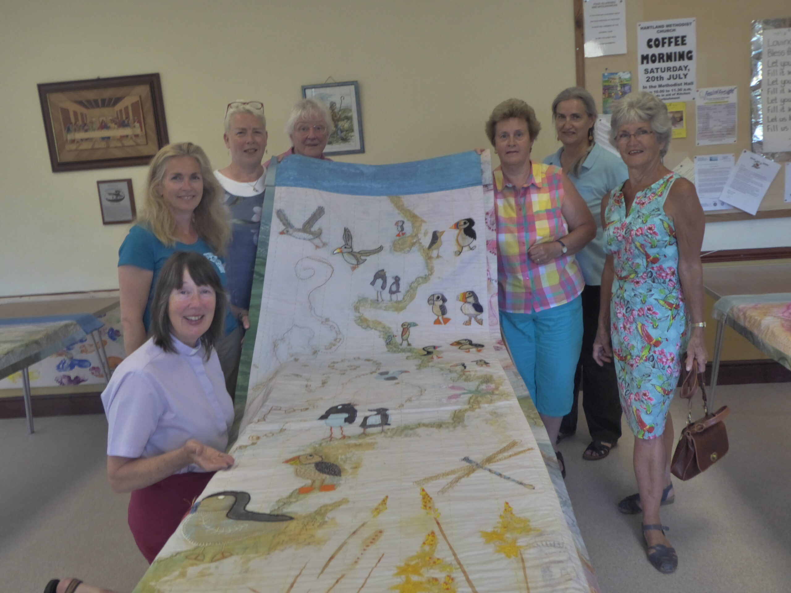 A group assembled to stitch at Hartland, aching backs from leaning over the banner and embroidering are forgotten when the end result is enjoyed.